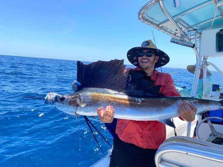 Man proudly holding a large sailfish on a boat, enjoying a successful fishing trip with Salty Dog Fishing Charters-Johns Pass-Treasure Island.
