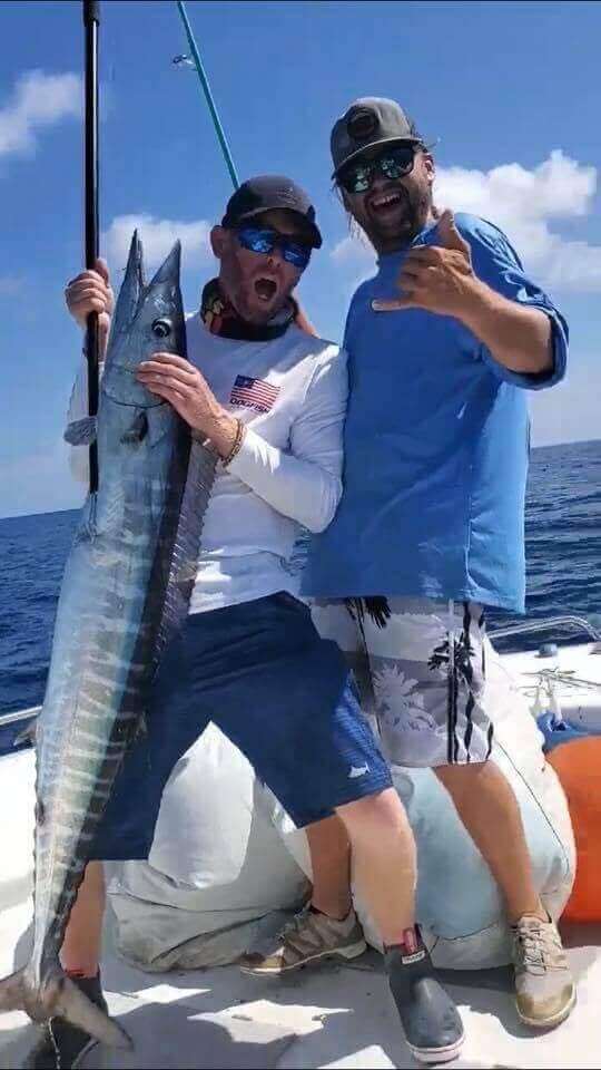 Two men proudly display a large fish on a boat under clear skies, only with Salty Dog Fishing Charters-Johns Pass-Treasure Island.