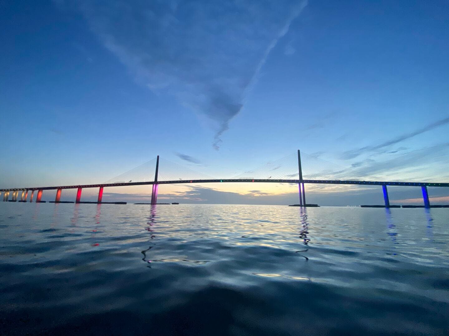 Colorful lit bridge over calm waters at sunset, only available at Salty Dog Fishing Charters-Johns Pass-Treasure Island.