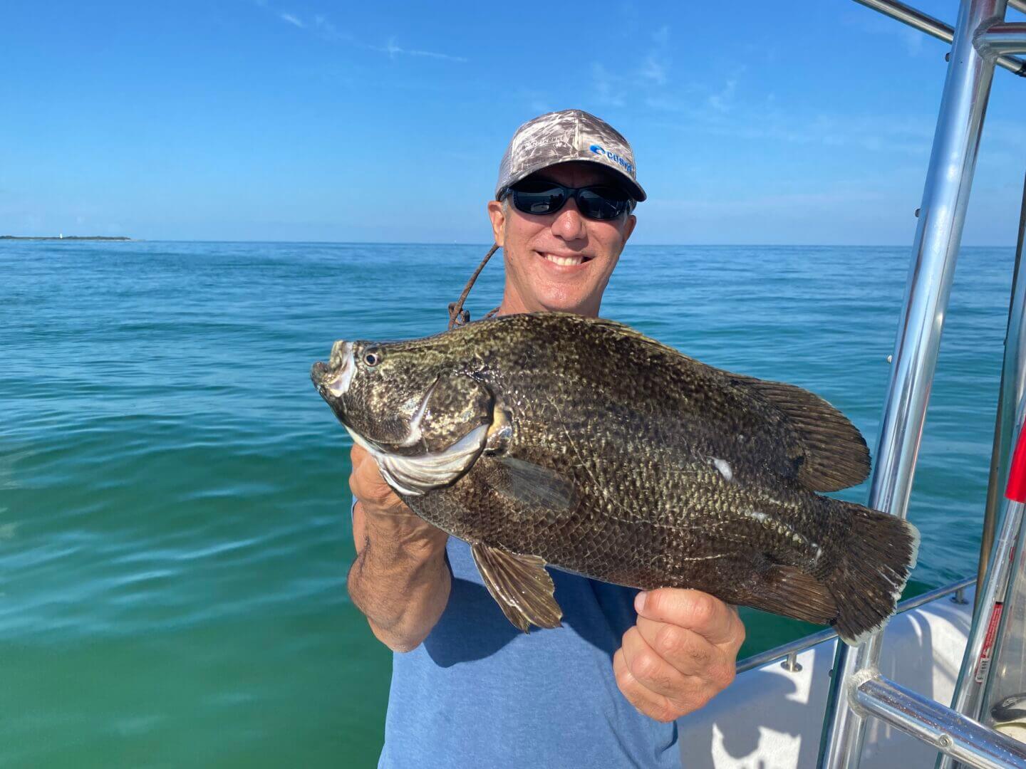 Man proudly holding a large fish on a boat, enjoying a sunny day at sea, only available at Salty Dog Fishing Charters-Johns Pass-Treasure Island.